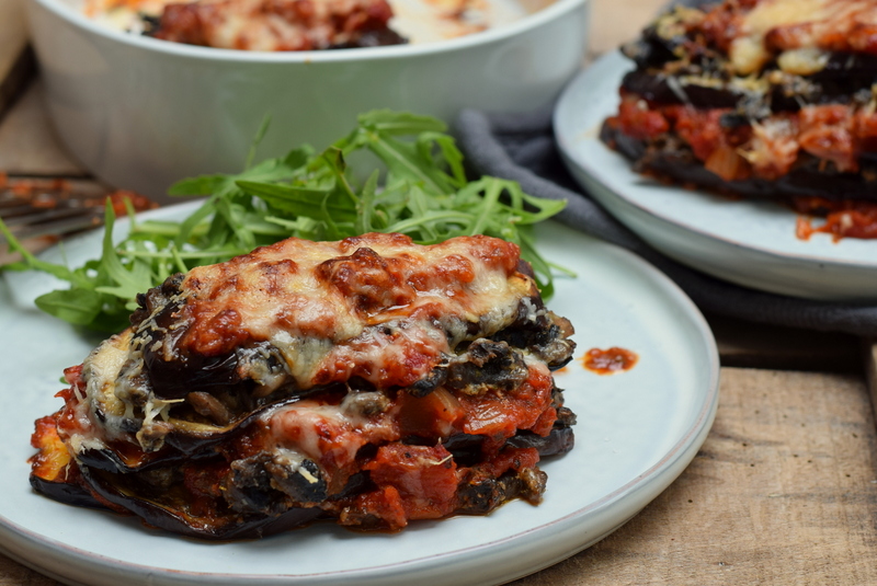 Zijaanzicht een wit bord met auberginelasagne met champignons en een groene salade