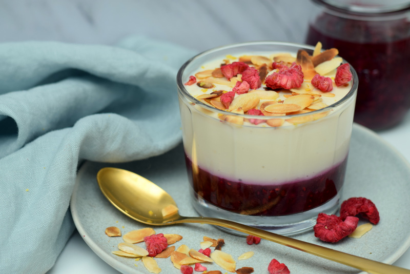 Zijaanzicht: rechts een bord met een glaasje citroenpudding met rode vruchten en een gouden lepel links een servette