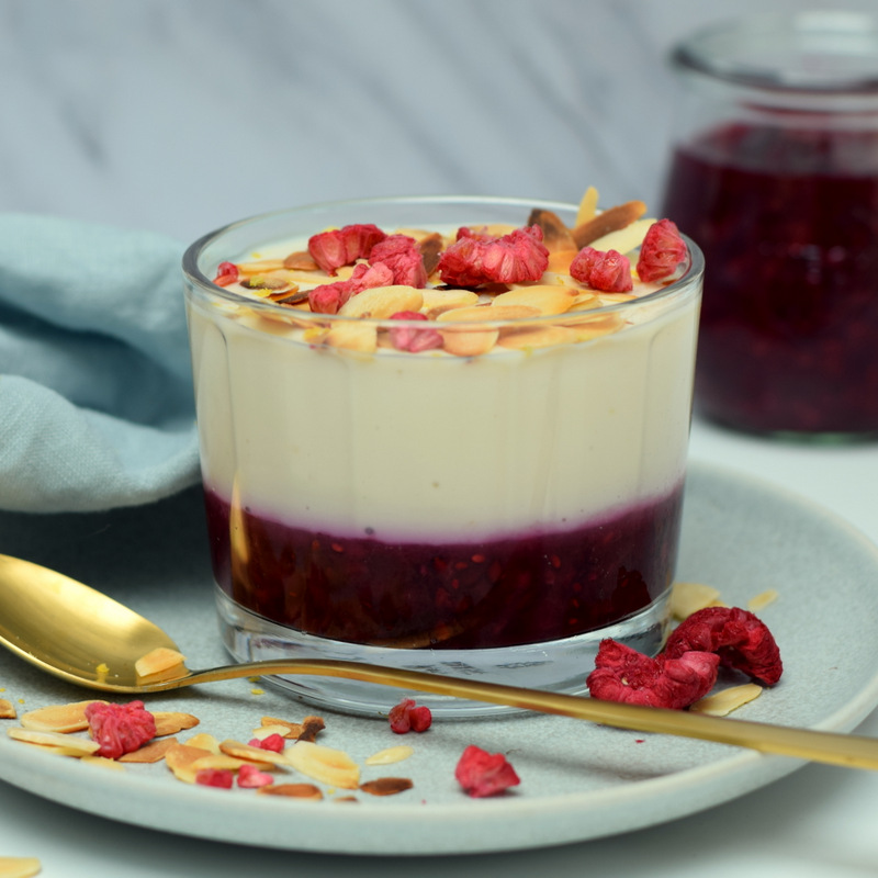 Zijaanzicht: een bord met een glaasje citroenpudding met rode vruchten en een gouden lepel