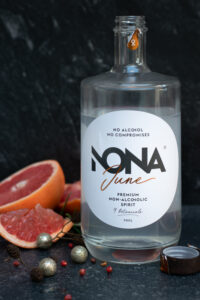 Zijaanzicht: een fles NONA June met links een gesneden pompelmoes