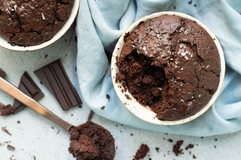 Bovenaanzicht 2 chocoladecakejes uit een potje links een lepel met een schepje cake en stukjes chocolade