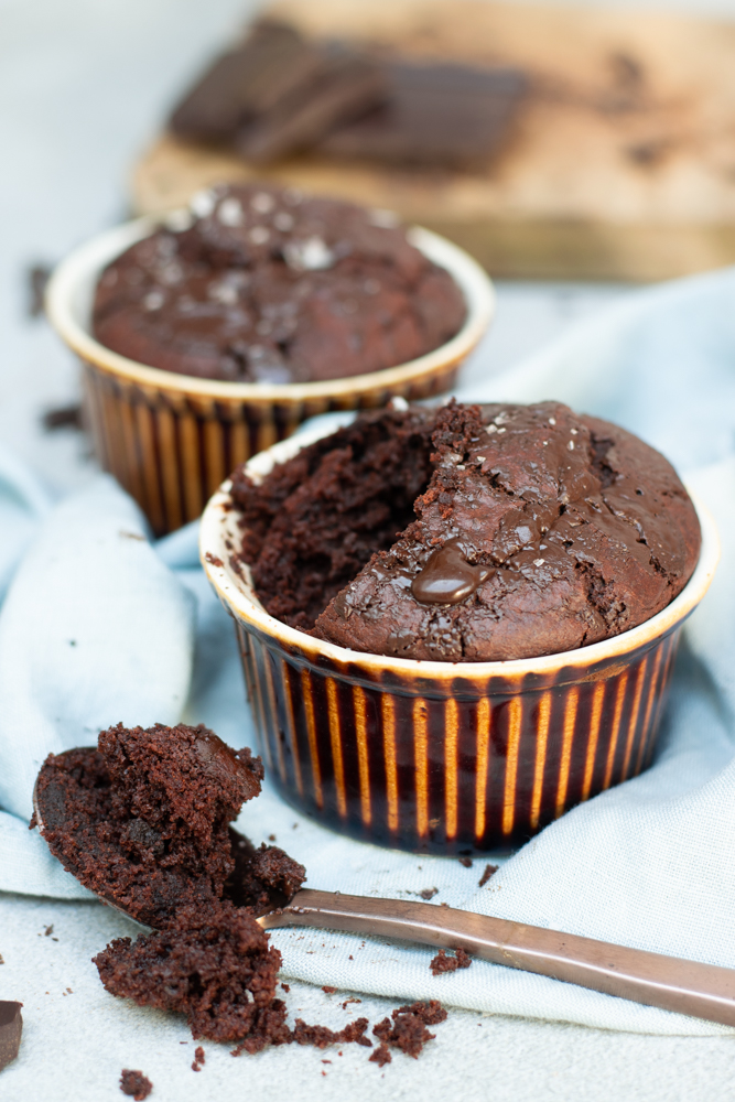 Zijaanzicht 2 chocoladecakejes uit een potje vooraan een lepel met een schepje cake