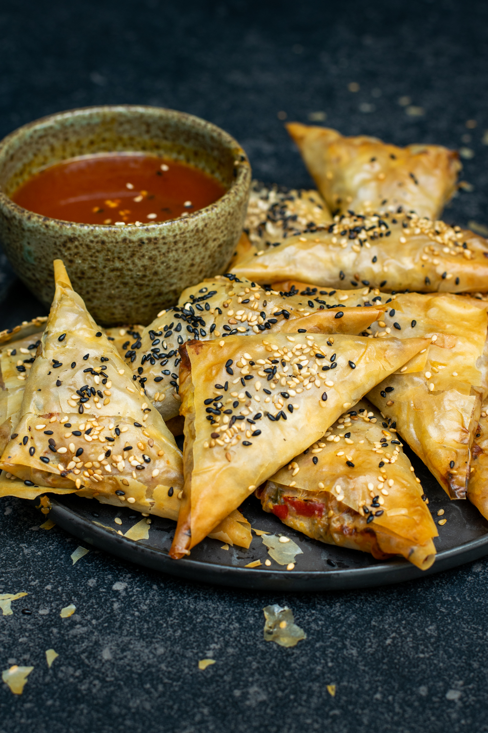 Zijaanzicht van een stapel loempia's op een donker bord, op een donkere achtergrond. Geserveerd met een potje zoetzure saus.