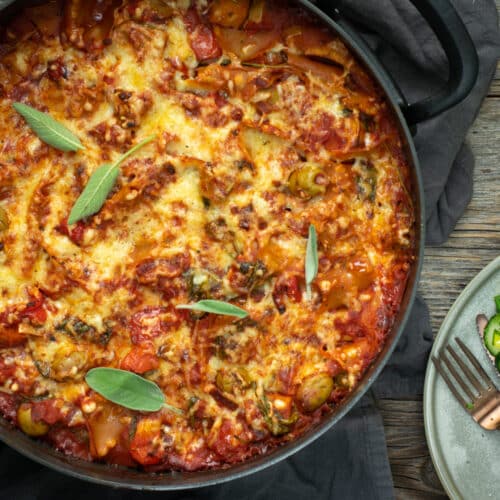 Bovenaanzicht van een gegratineerde lasagne, in een zwarte, ronde ovenschotel, op een houten ondergrond.