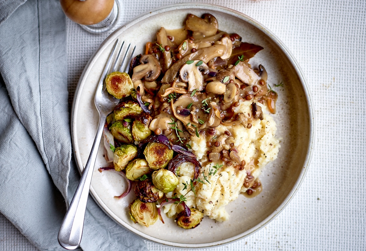 Bovenaanzicht van een wit bord gevuld met champignonragout, knolselderpuree en geroosterde spruitjes